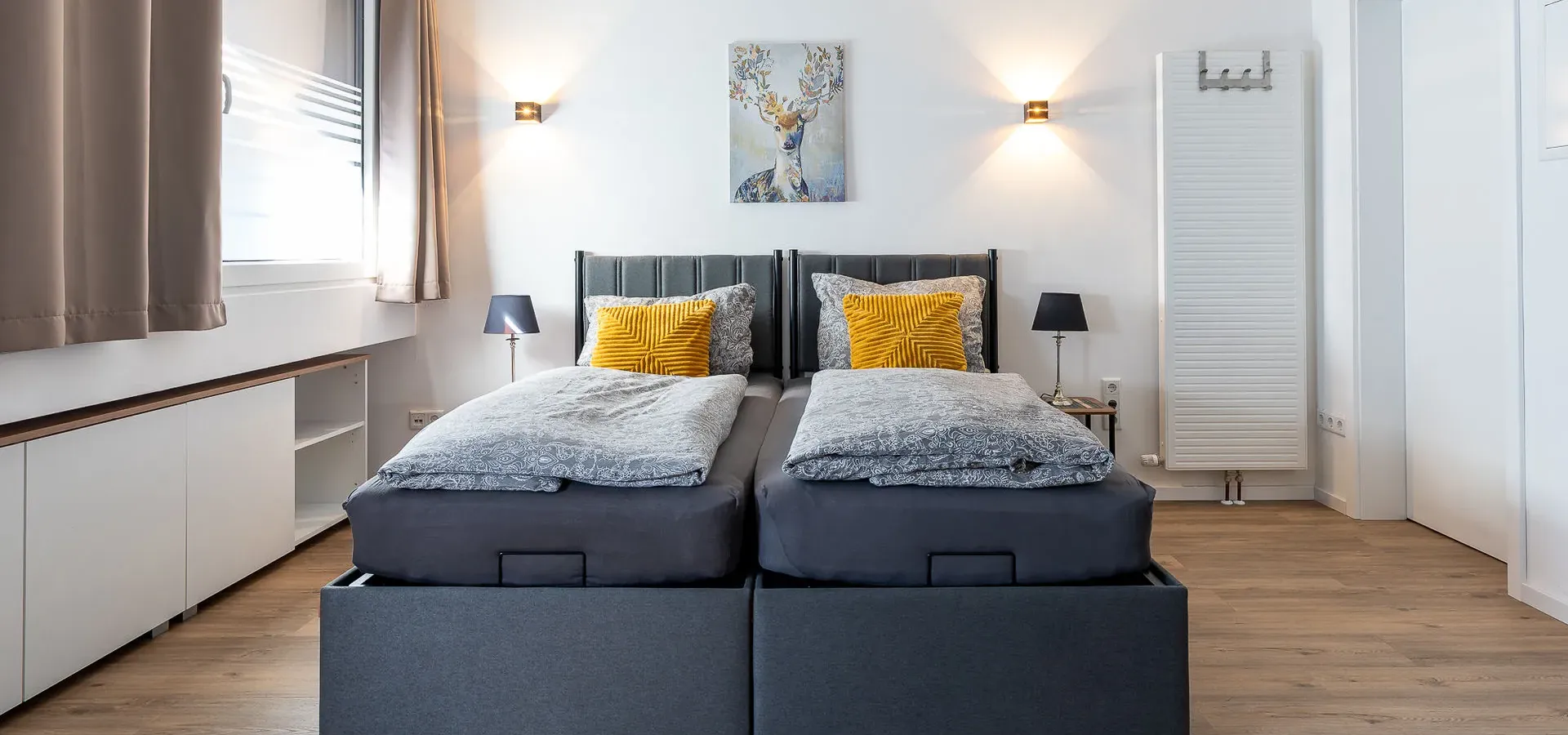 Schlafzimmer in Apartment 1 mit zwei Betten, gelben Kissen und Hirschbild